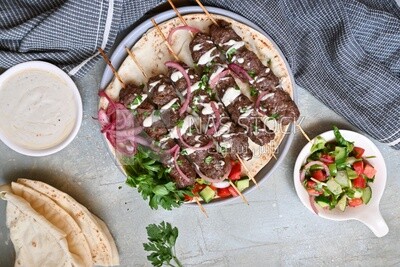 Dish with grilled kofta next to two plates of salads