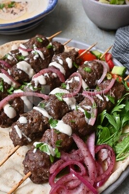 Dish with grilled kofta with tahini sauce on it