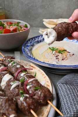Hand holding grilled kofta with tahini