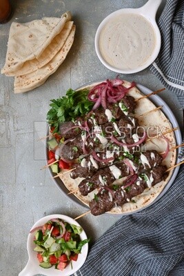 Dish with grilled kofta next to two plates of salads