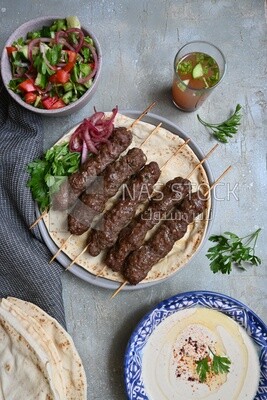 Dish with grilled kofta next to two plates of salads