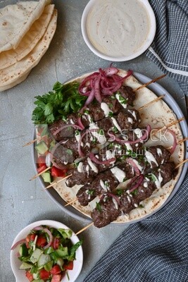 Dish with grilled kofta next to two plates of salads