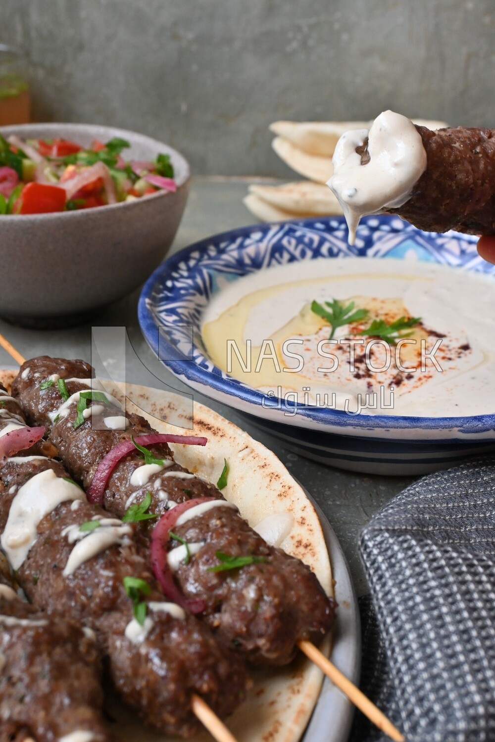 Hand holding grilled kofta with tahini