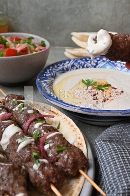 Hand holding grilled kofta with tahini