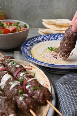 Hand holding grilled kofta with tahini