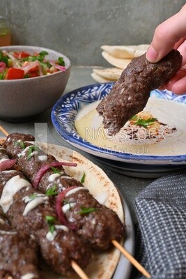 Hand holding grilled kofta with tahini