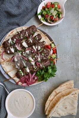 Dish with grilled kofta next to two plates of salads