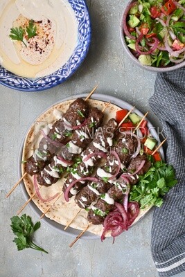 Dish with grilled kofta next to two plates of salads