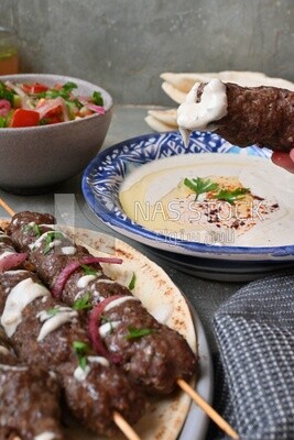 Hand holding grilled kofta with tahini
