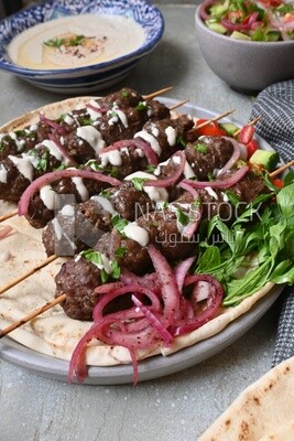 Dish with grilled kofta with tahini sauce on it