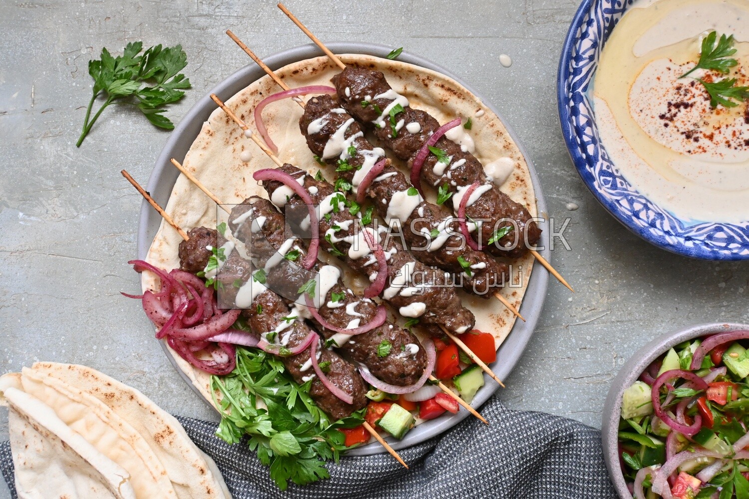 Dish with grilled kofta next to two plates of salads
