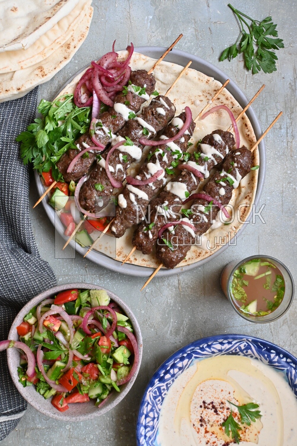 Dish with grilled kofta next to two plates of salads