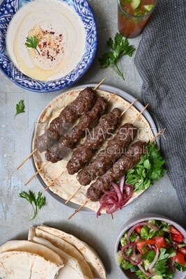 Dish with grilled kofta next to two plates of salads