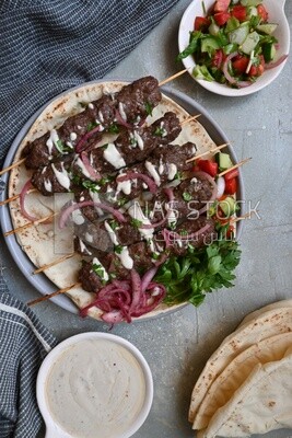 Dish with grilled kofta next to two plates of salads