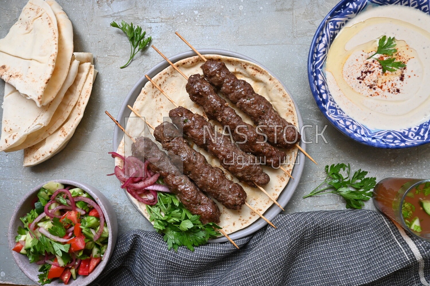 Dish with grilled kofta next to two plates of salads