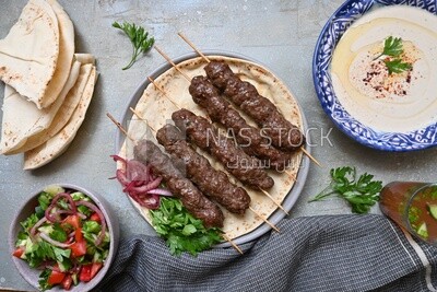 Dish with grilled kofta next to two plates of salads