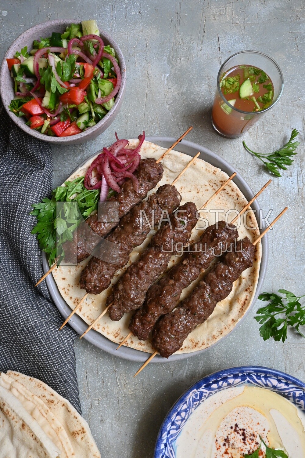 Dish with grilled kofta next to two plates of salads