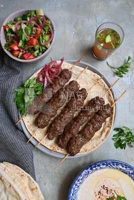 Dish with grilled kofta next to two plates of salads