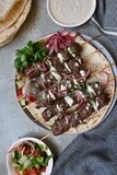 Dish with grilled kofta next to two plates of salads