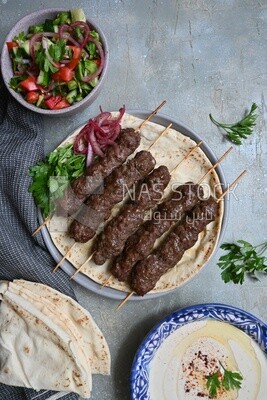 Dish with grilled kofta next to two plates of salads