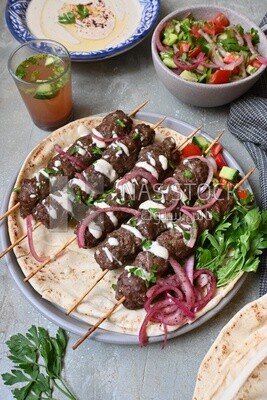 Dish with grilled kofta next to two plates of salads