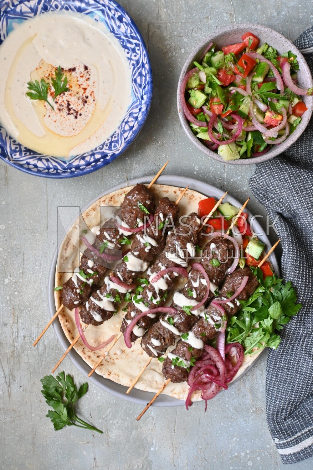 Dish with grilled kofta next to two plates of salads