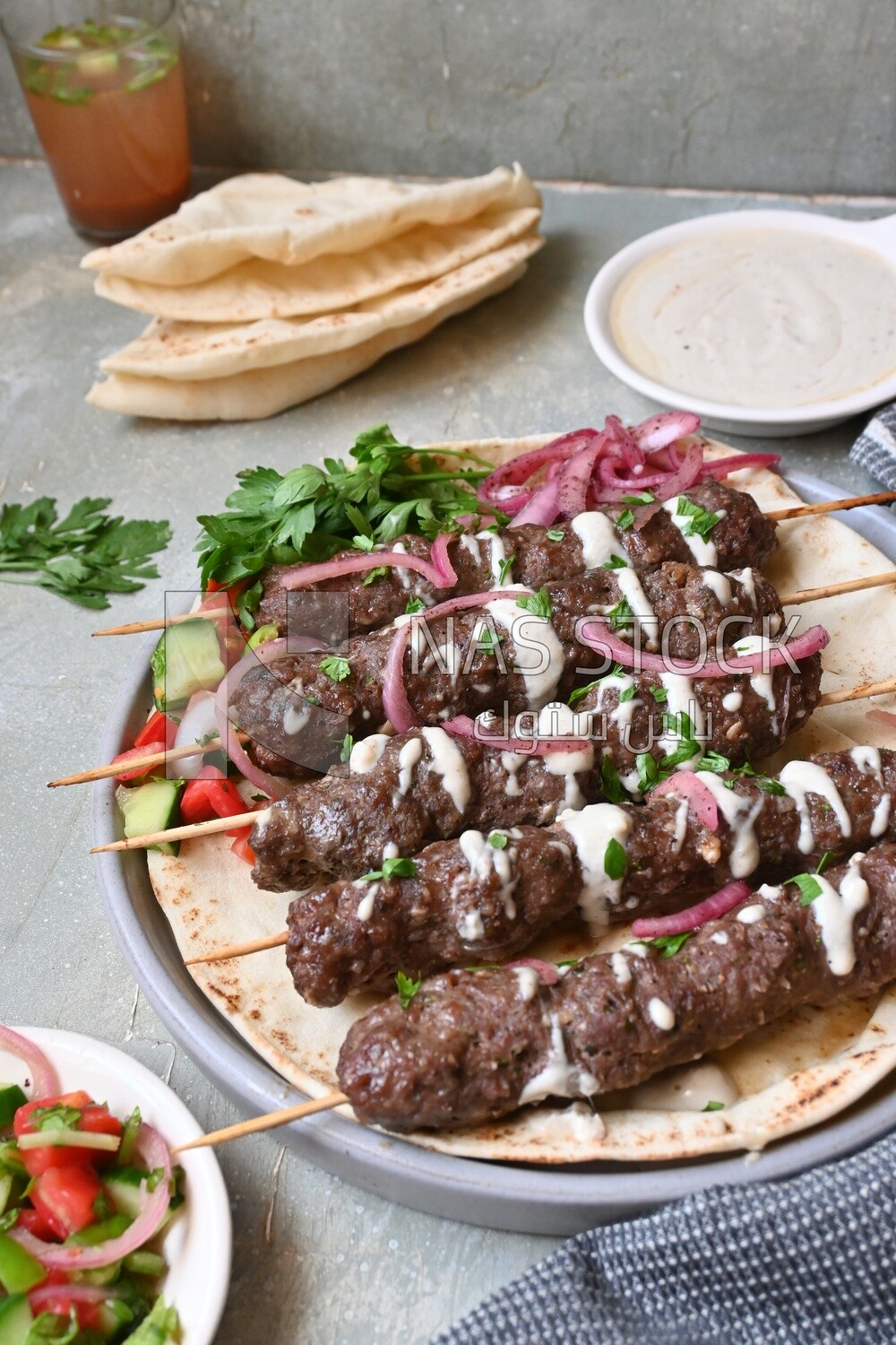 Dish with grilled kofta next to two plates of salads