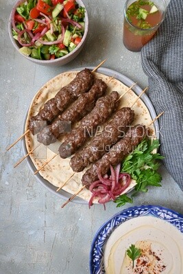 Dish with grilled kofta next to two plates of salads