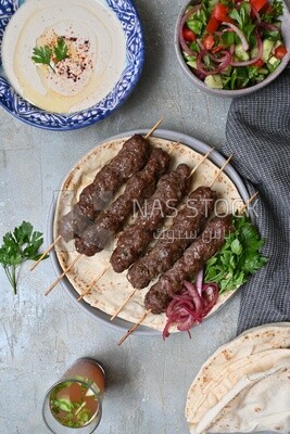 Dish with grilled kofta next to two plates of salads