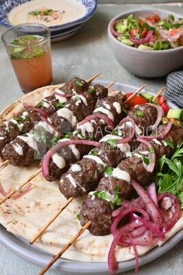 Dish with grilled kofta next to two plates of salads