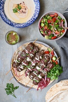 Dish with grilled kofta next to two plates of salads