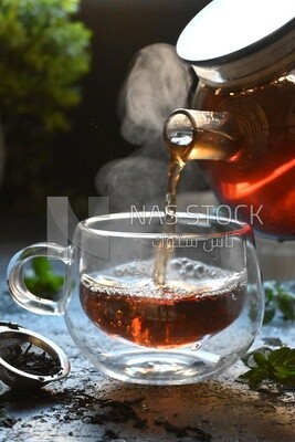 Glass kettle pouring tea from jug to cup of tea