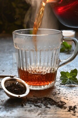 Glass kettle pouring tea from jug to cup of tea