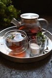 Cup of tea with a glass kettle, sugar, and a mint on a tray