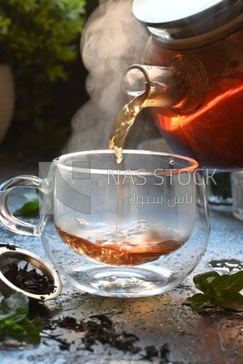 Glass kettle pouring tea from jug to cup of tea