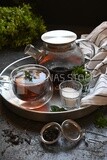 Cup of tea with a glass kettle, sugar, and a mint on a tray