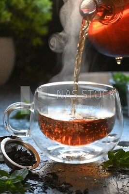 Glass kettle pouring tea from jug to cup of tea