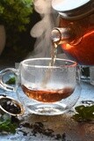 Glass kettle pouring tea from jug to cup of tea