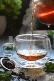 Glass kettle pouring tea from jug to cup of tea