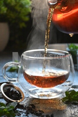 Glass kettle pouring tea from jug to cup of tea