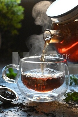 Glass kettle pouring tea from jug to cup of tea