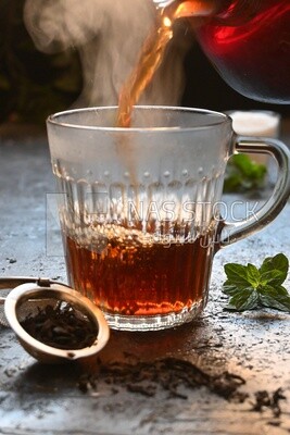Glass kettle pouring tea from jug to cup of tea