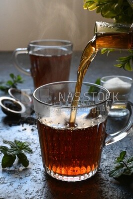Glass kettle pouring tea from jug to cup of tea