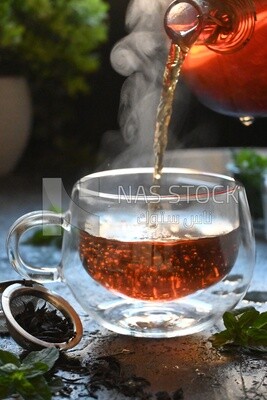 Glass kettle pouring tea from jug to cup of tea