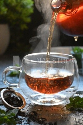 Glass kettle pouring tea from jug to cup of tea