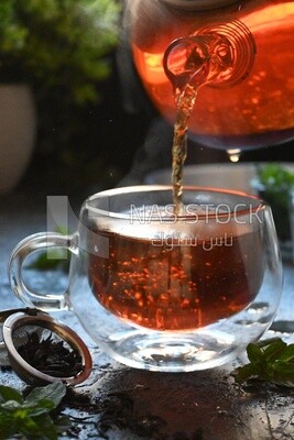 Glass kettle pouring tea from jug to cup of tea