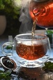 Glass kettle pouring tea from jug to cup of tea