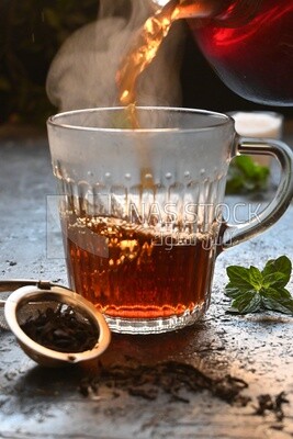 Glass kettle pouring tea from jug to cup of tea