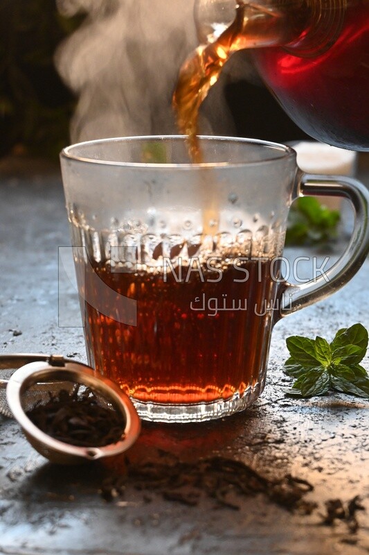 Glass kettle pouring tea from jug to cup of tea