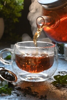 Glass kettle pouring tea from jug to cup of tea